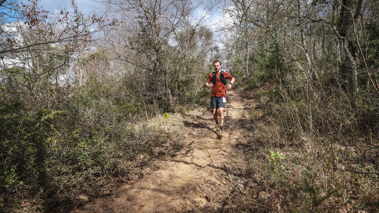 Trailrunner op een breed, modderig pad door kaal voorjaarsbos tijdens de Chianti Marathon Trail
