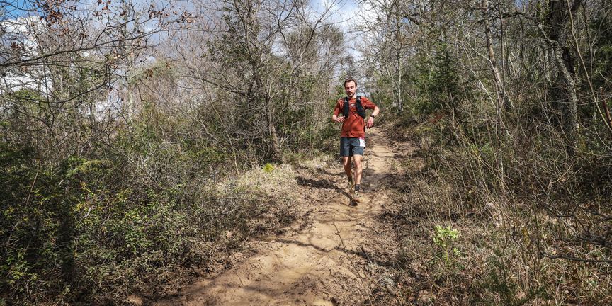 Trailrunner op een breed, modderig pad door kaal voorjaarsbos tijdens de Chianti Marathon Trail