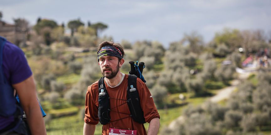 Hardloper met wedstrijdnummer en trailvest tijdens de Chianti-trail, Toscaanse heuvels op de achtergrond