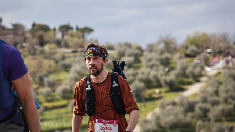 Hardloper met wedstrijdnummer en trailvest tijdens de Chianti-trail, Toscaanse heuvels op de achtergrond