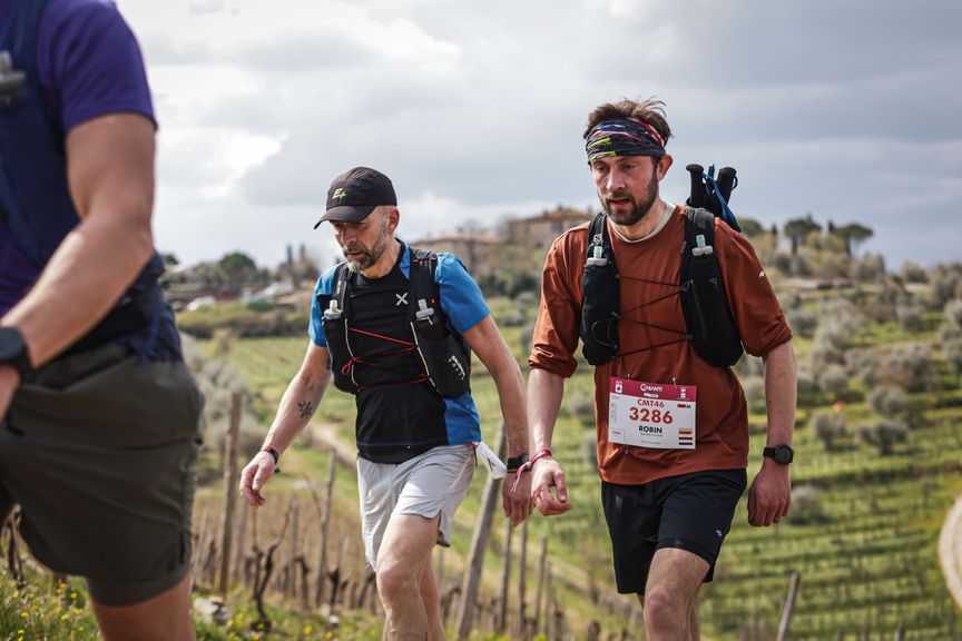 Twee trailrunners wandelen een klim op door de Toscaanse wijngaarden tijdens de Chianti Marathon Trail