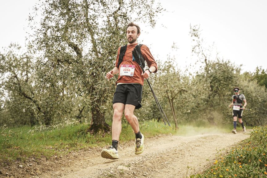 Trailrunner met loopstokken op een stoffig pad door een olijfgaard tijdens de Chianti Marathon Trail