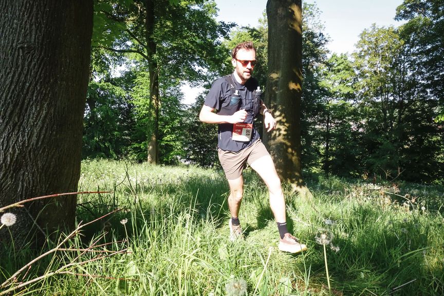Hardloper met rugnummer 943 loopt door hoog gras tussen grote bomen in zonnig bos
