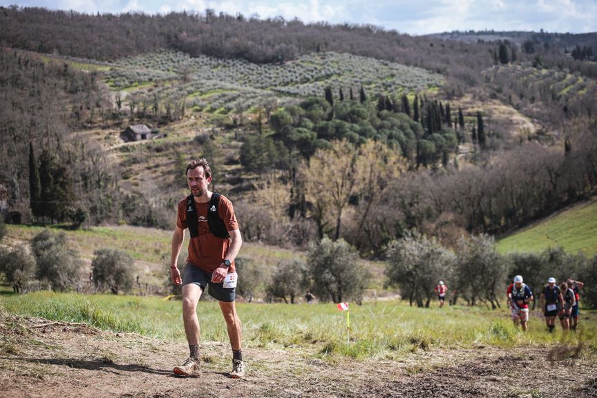 Hardloper met wedstrijdnummer klimt door de Chianti-heuvels tijdens een trailrace