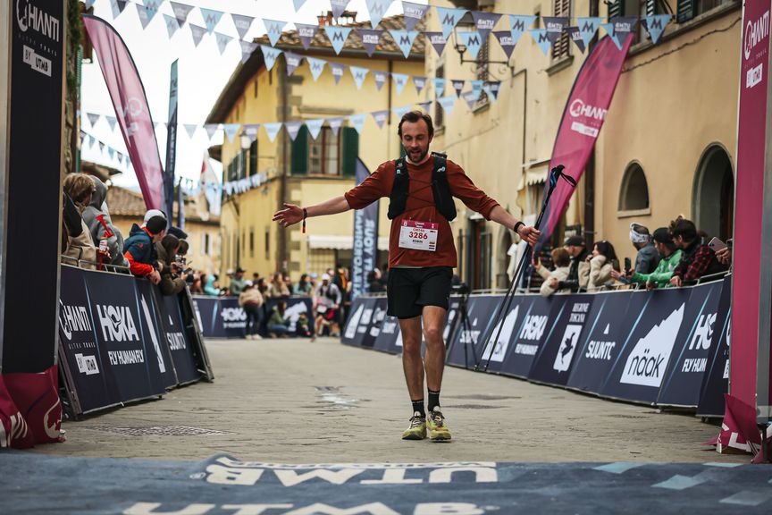 Hardloper met rugnummer 3286 komt over de finish op een geplaveide straat, met Chianti Ultra Trail-vlaggen langs de kant