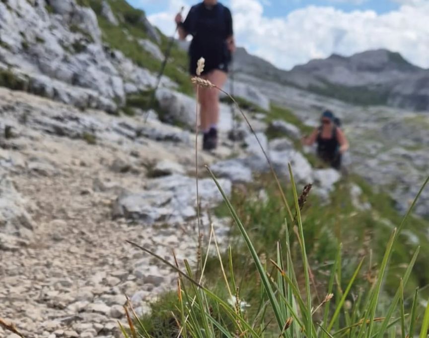 Twee wandelaars klimmen over een rotsachtig bergpad, met pieken op de achtergrond