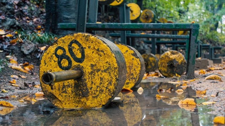 Verweerde gele halter met '80' erop, liggend in de modder bij een openluchtgym in het bos