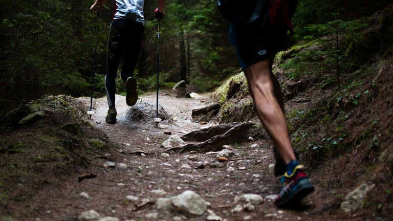 Benen van twee trailrunners met stokken op een rotsachtig bospad
