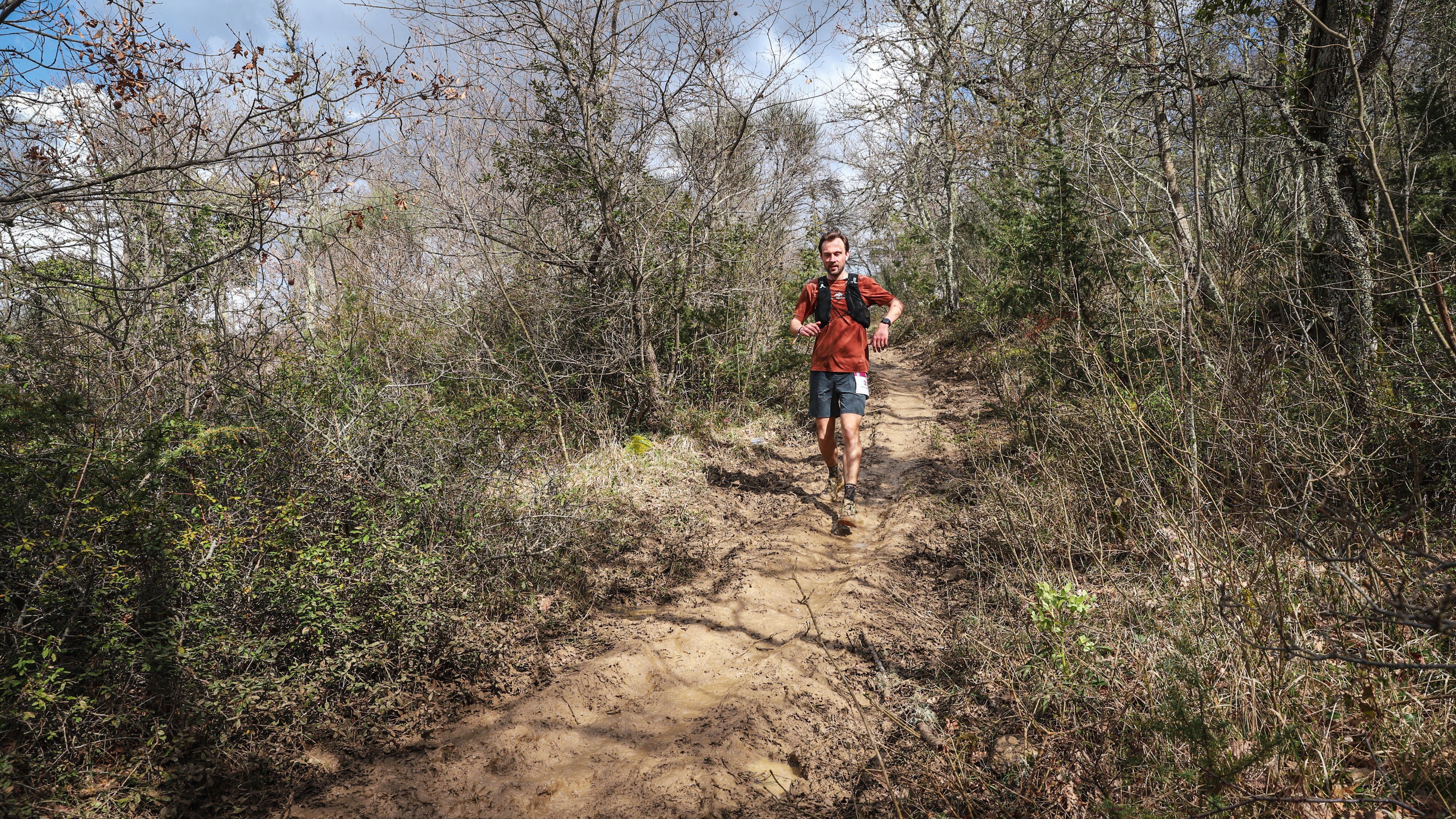 Trailrunner op een breed, modderig pad door kaal voorjaarsbos tijdens de Chianti Marathon Trail