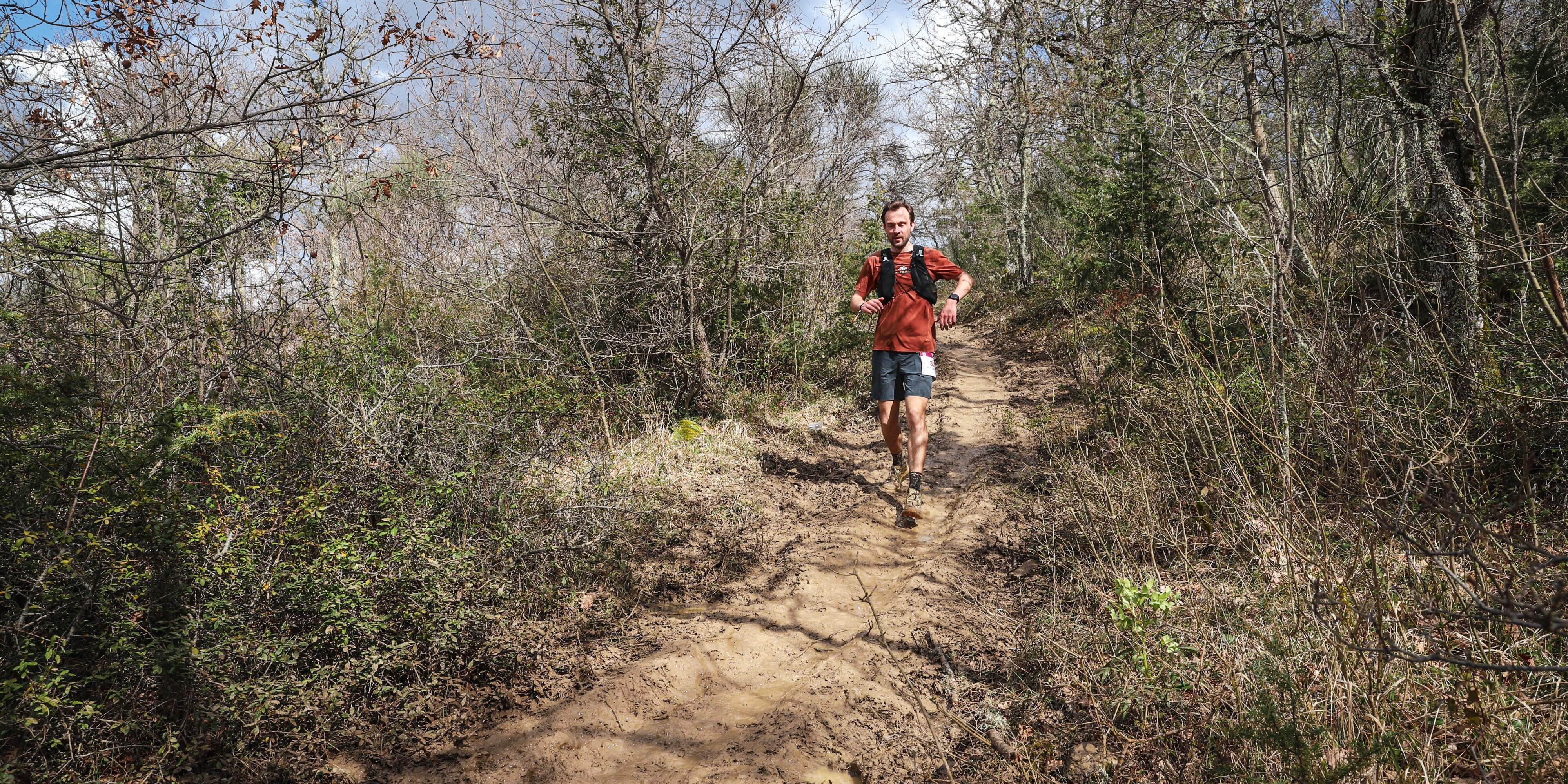 Trailrunner op een breed, modderig pad door kaal voorjaarsbos tijdens de Chianti Marathon Trail