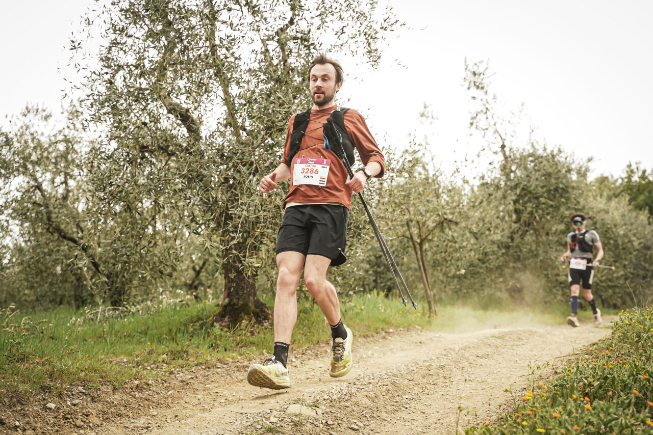 Trailrunner met loopstokken op een stoffig pad door een olijfgaard tijdens de Chianti Marathon Trail